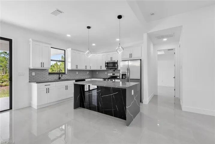 Contemporary kitchen featuring a large black marble island with white veining, white cabinetry, stainless steel appliances, and a gray subway tile backsplash