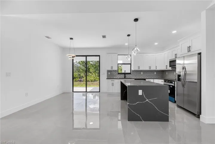 Contemporary kitchen featuring white cabinetry, a dark waterfall island with veining, stainless steel appliances, and a gray subway tile backsplash
