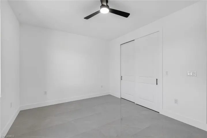 Spacious room featuring modern tile flooring, crisp white walls, a contemporary ceiling fan, and sliding panel closet doors with black hardware