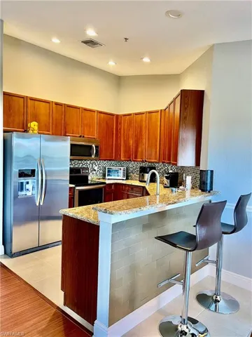 Kitchen featuring light stone counters, a peninsula, stainless steel appliances, and tasteful backsplash