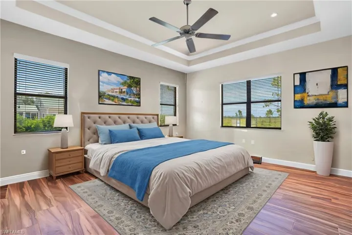 Bedroom with ceiling fan, multiple windows, a tray ceiling, and wood-type flooring