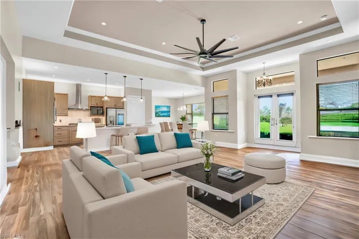 Living room with light hardwood / wood-style flooring, ceiling fan with notable chandelier, french doors, and a tray ceiling