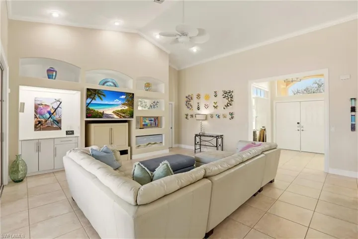 Living room featuring built in features, a ceiling fan, vaulted ceiling, crown molding, and light tile patterned floors