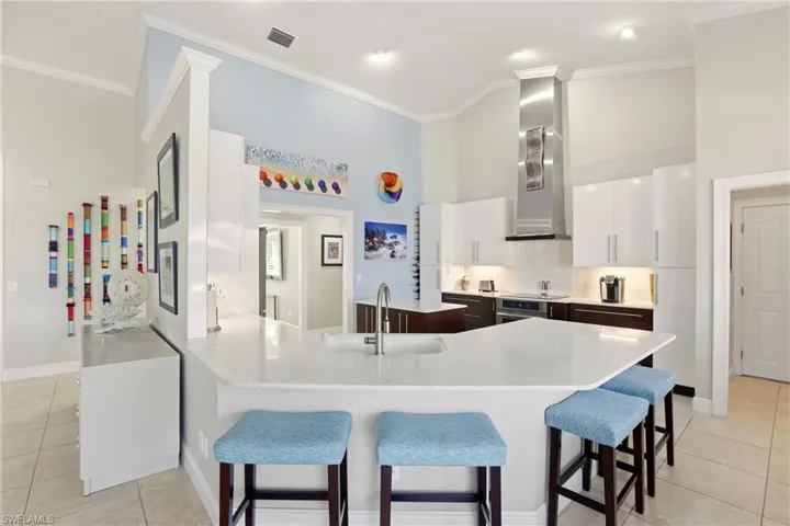 Two tone kitchen with dual tone cabinets, light tile patterned flooring, a peninsula, a kitchen bar, and backsplash