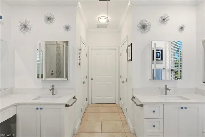Bathroom with two vanities, a shower stall, crown molding, and light tile patterned flooring