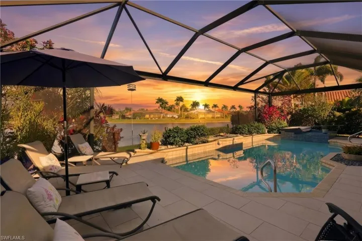 Pool at dusk featuring glass enclosure, a patio area, a sunroom, and a pool with connected hot tub