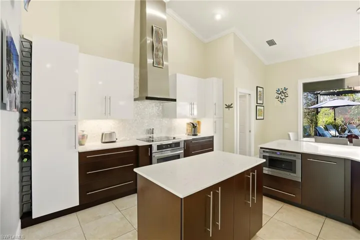 Kitchen featuring backsplash, two tone cabinetry, a kitchen island, oven, and light tile patterned floors