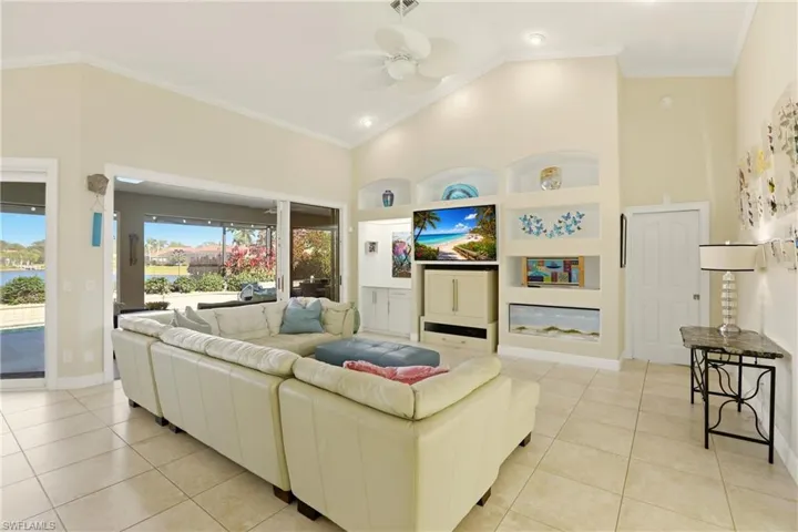 Living room with built in shelves, a ceiling fan, crown molding, vaulted ceiling, and light tile patterned floors