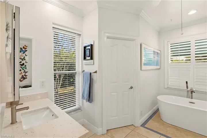 Full bathroom featuring a freestanding tub, light tile patterned floors, crown molding, and vanity