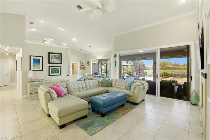 Living area with ceiling fan, light tile patterned floors, recessed lighting, ornamental molding, and lofted ceiling