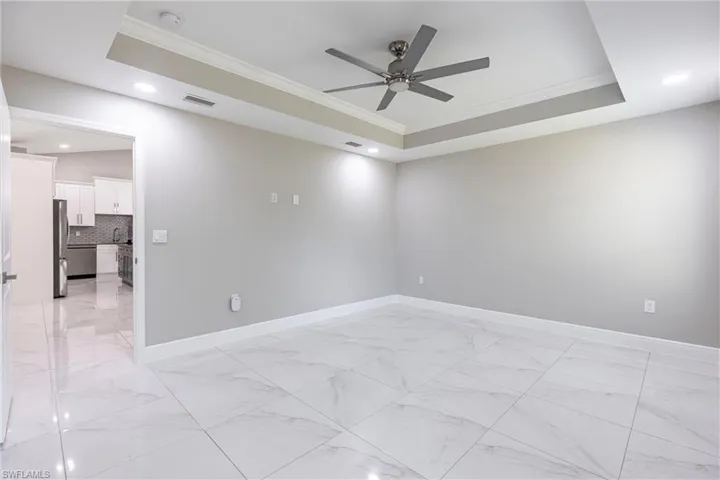 Unfurnished room featuring light marble finish flooring, ornamental molding, a raised ceiling, a ceiling fan, and recessed lighting