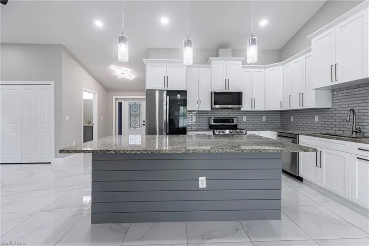 Kitchen featuring stainless steel appliances, backsplash, light marble finish floors, white cabinets, and a kitchen island