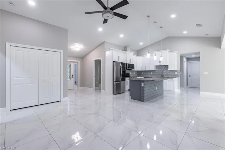 Kitchen featuring decorative backsplash, white cabinetry, appliances with stainless steel finishes, light marble finish floors, and a center island