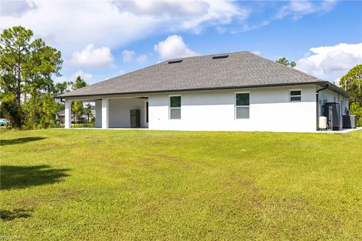 Back of property with a lawn, stucco siding, and roof with shingles