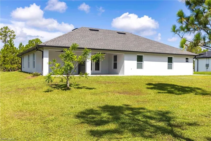 Back of property featuring a lawn, stucco siding, and a shingled roof