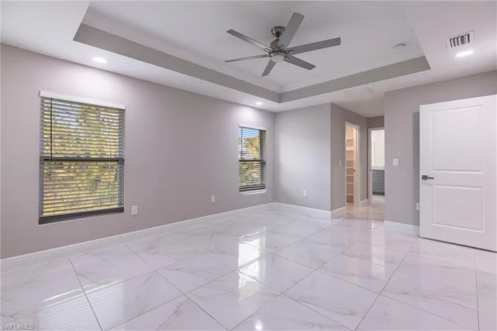 Empty room with a tray ceiling, light marble finish flooring, ornamental molding, ceiling fan, and recessed lighting
