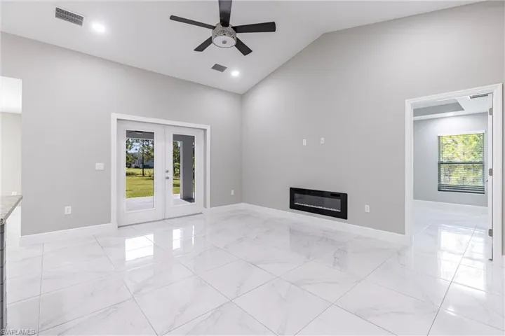 Unfurnished living room with french doors, a glass covered fireplace, light marble finish flooring, healthy amount of natural light, and high vaulted ceiling