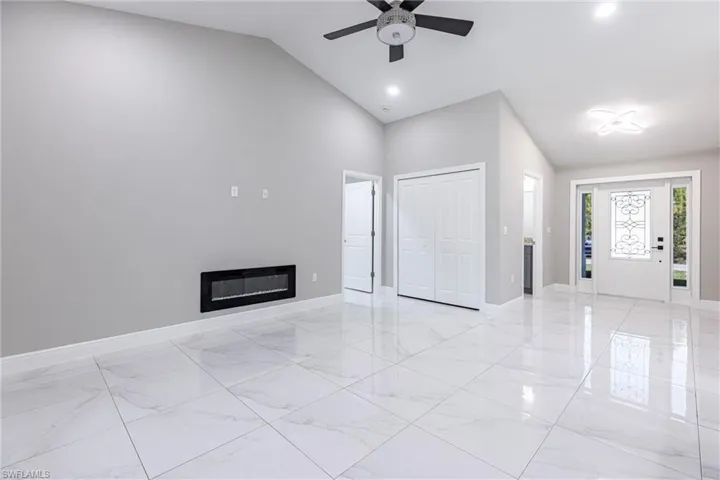 Unfurnished living room with light marble finish flooring, a glass covered fireplace, high vaulted ceiling, a ceiling fan, and recessed lighting
