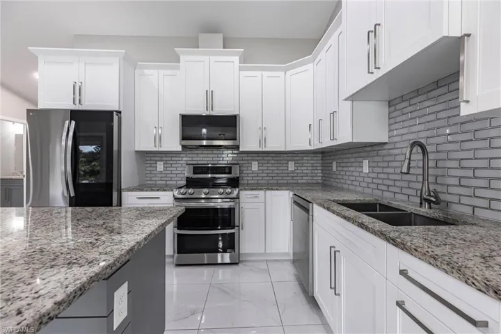 Kitchen featuring appliances with stainless steel finishes, backsplash, white cabinetry, and light stone countertops