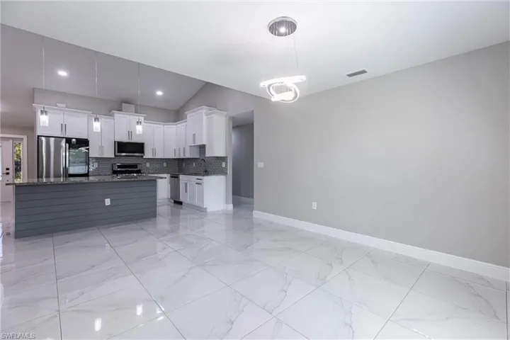 Kitchen featuring appliances with stainless steel finishes, light marble finish flooring, decorative backsplash, white cabinetry, and hanging light fixtures