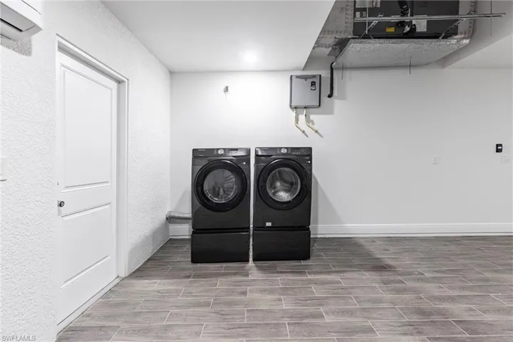 Laundry room with separate washer and dryer, wood tiled floors, and an AC wall unit