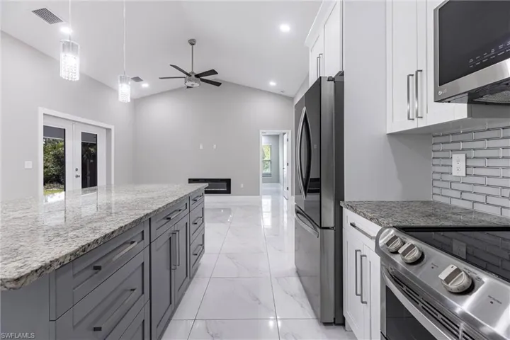 Kitchen featuring appliances with stainless steel finishes, white cabinetry, light stone countertops, tasteful backsplash, and light marble finish floors