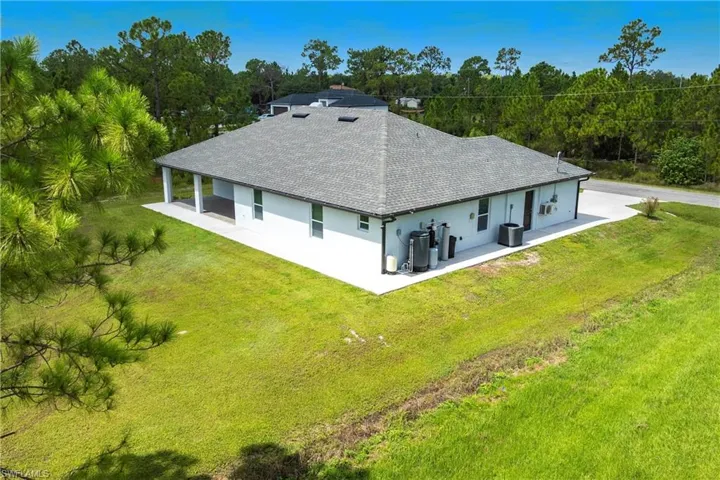 Back of property featuring a patio, a shingled roof, stucco siding, and a yard