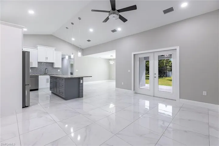 Kitchen featuring french doors, backsplash, light marble finish flooring, white cabinetry, and lofted ceiling