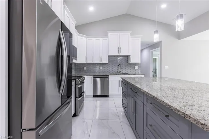 Kitchen with stainless steel appliances, tasteful backsplash, light marble finish floors, white cabinetry, and light stone counters