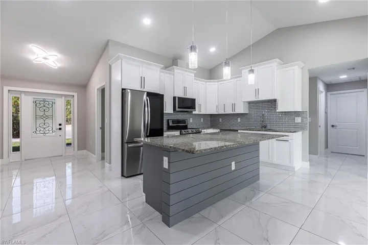 Kitchen with appliances with stainless steel finishes, backsplash, stone counters, light marble finish flooring, and white cabinetry
