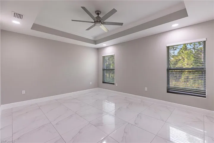 Empty room featuring a tray ceiling, light marble finish floors, crown molding, recessed lighting, and a ceiling fan