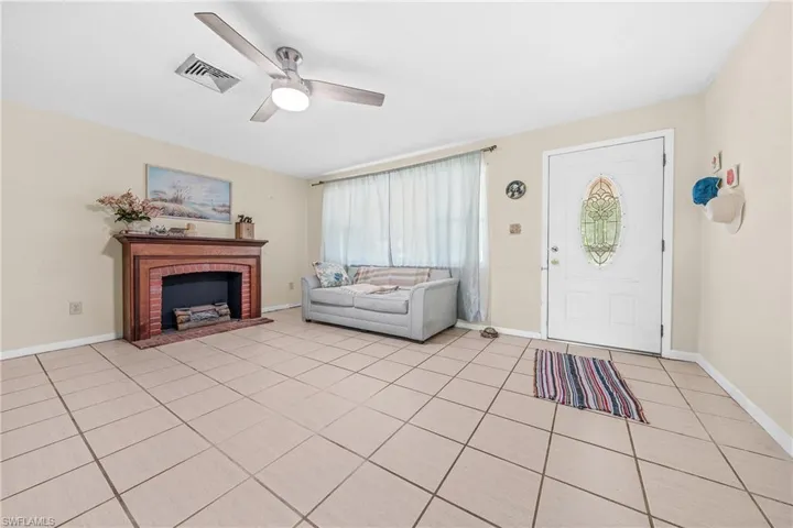 Entrance foyer with ceiling fan, light tile patterned floors, and a brick fireplace