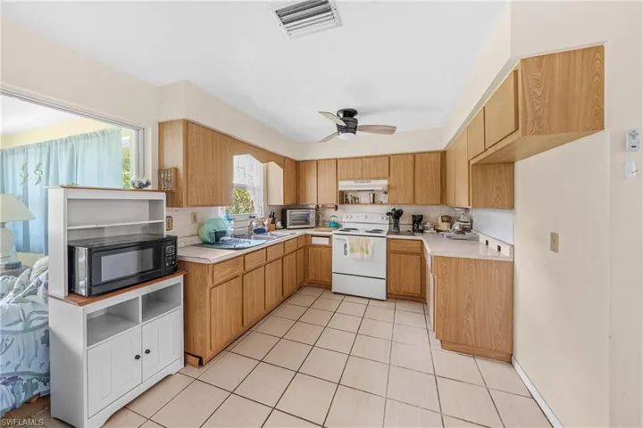 Kitchen featuring white electric range, black microwave, under cabinet range hood, backsplash, and light countertops
