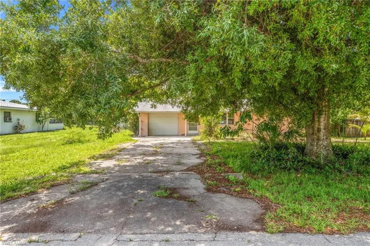 View of property hidden behind natural elements with asphalt driveway, a garage, and a front yard