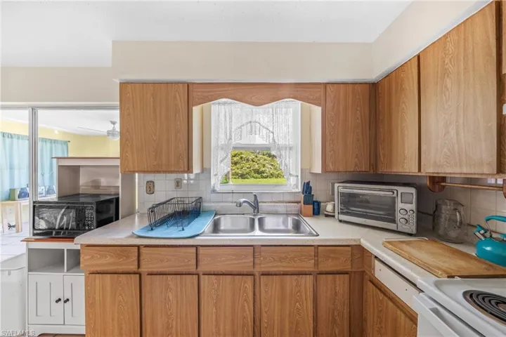 Kitchen featuring black microwave, light countertops, decorative backsplash, brown cabinets, and stove