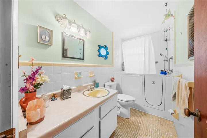 Bathroom with vanity, tile patterned flooring, tile walls, wainscoting, and a shower
