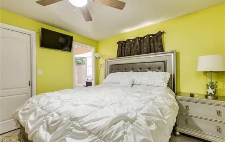 Bedroom featuring a ceiling fan, wall-mounted television, and an upholstered headboard