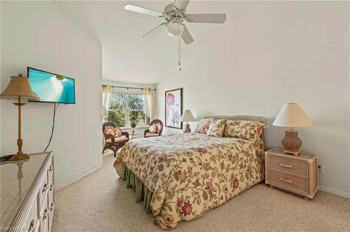 The primary bedroom with ceiling fan, light colored carpet, and lofted ceiling