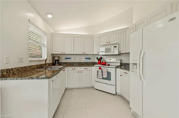 Kitchen featuring lofted ceiling, white appliances, sink, light tile patterned floors, and white cabinetry