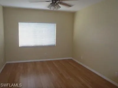 Spacious bedroom featuring wood-finish flooring, neutral wall finishes, ceiling fan with integrated lighting, and a large window with horizontal blinds providing natural light