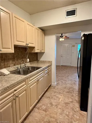Kitchen with freestanding refrigerator, backsplash, light brown cabinetry, and ceiling fan