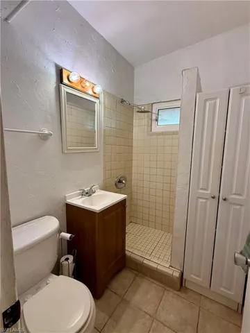 Bathroom with a textured wall, vanity, a shower stall, light tile patterned flooring, and a closet
