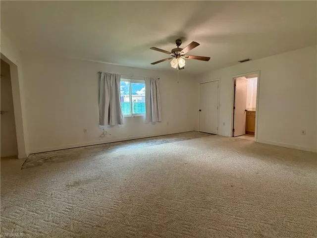 Unfurnished bedroom with light carpet, ceiling fan, and connected bathroom