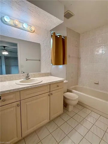 Full bath with light tile patterned floors, vanity, and washtub / shower combination