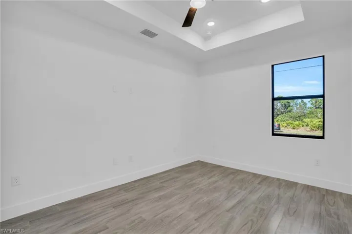 Unfurnished room featuring a tray ceiling, ceiling fan, and light hardwood / wood-style floors