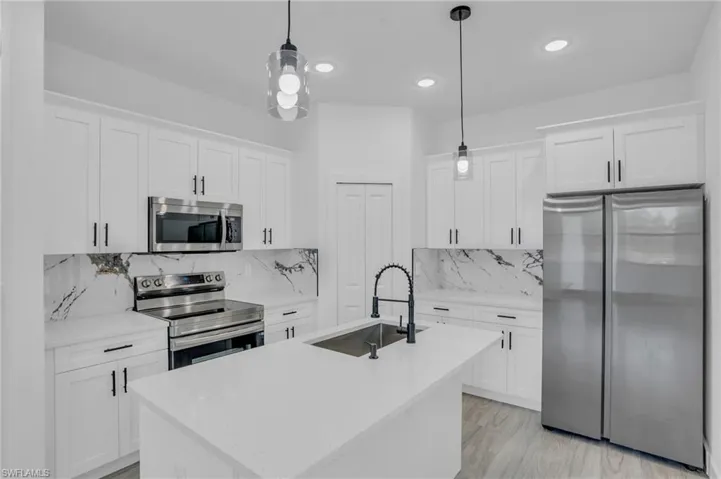Kitchen with white cabinetry, sink, stainless steel appliances, and decorative light fixtures