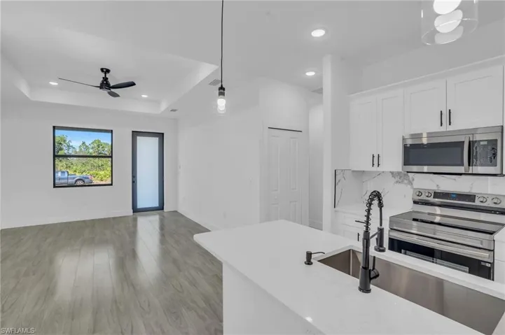 Kitchen featuring white cabinets, a raised ceiling, hanging light fixtures, light hardwood / wood-style floors, and stainless steel appliances