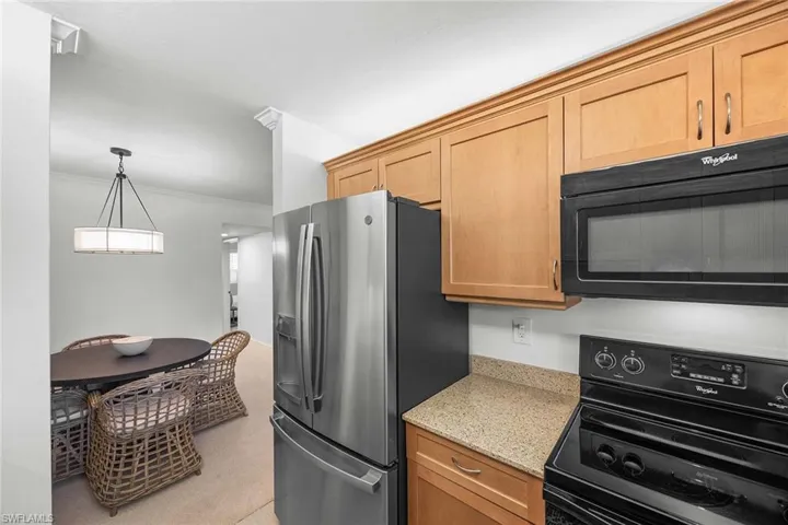 Kitchen with black appliances, light stone counters, crown molding, decorative light fixtures, and light carpet