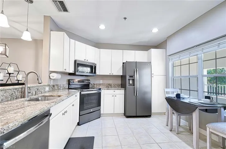 Kitchen featuring stainless steel appliances, light stone counters, hanging light fixtures, white cabinets, and light tile patterned floors