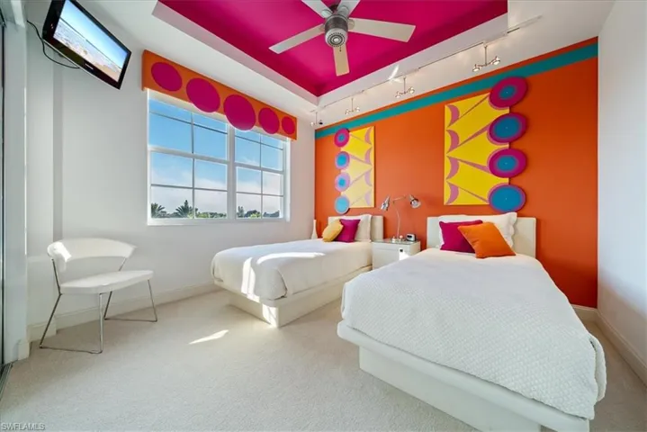 Carpeted bedroom with a tray ceiling, multiple windows, track lighting, and a ceiling fan